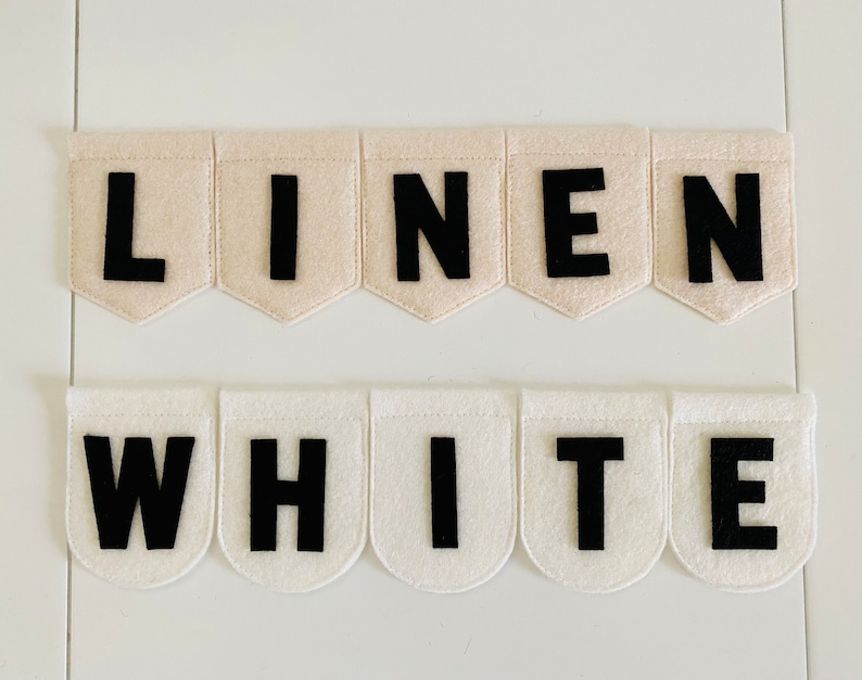 May include: Two banners with the words "LINEN" and "WHITE" spelled out in black letters on cream and white felt pennants. The pennants are arranged in two rows against a white background.