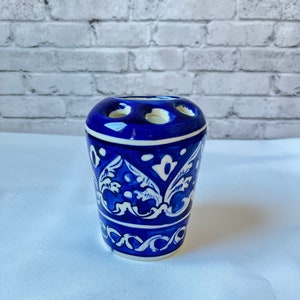 May include: Blue and white ceramic toothbrush holder with a floral design. The holder has four slots for toothbrushes.