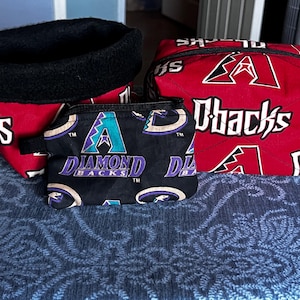 May include: A set of three fabric items featuring the Arizona Diamondbacks logo. Includes a red and black basket, a zippered cube, and a small pouch. The basket has a black fleece trim. The pouch is black with a Diamondbacks logo.