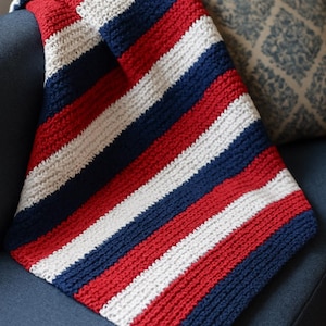 May include: A red, white and blue striped crocheted blanket. The blanket is folded and draped over a sofa.