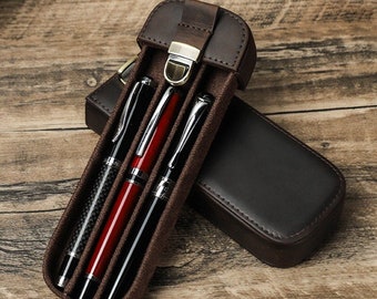 May include: A brown leather pen case with a flap closure and a metal clasp. The case holds three pens, one with a carbon fiber finish, one with a red finish, and one with a silver finish.