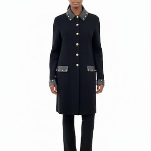 May include: A black coat with gold buttons, leather collar and pocket accents. The coat has long sleeves and a tailored fit. The model is wearing black pants and shoes. The coat is a classic design.