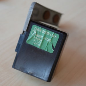 May include: A black timer door lock with a green label that reads "TIMER DOOR LOCK 38201 FC003 484593 NILES JAPAN".
