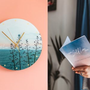 May include: A round glass clock with a blue and white sunset scene and gold hands. The clock face says "Self Love". A book with a blue and pink ombre cover says "Your Self Love Clock" and "It's time to truly love yourself".
