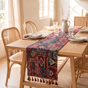 May include: A rectangular table runner featuring a multi-colored geometric pattern in shades of red, blue, and black. The fabric has a woven texture and is finished with decorative tassels in red, brown, and gold along the bottom edge.