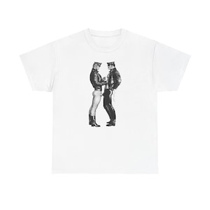 Puede incluir: Camiseta blanca con una ilustración en blanco y negro de dos figuras vestidas de cuero. Las figuras están representadas en un abrazo cercano. La camiseta tiene cuello redondo y la ilustración es detallada, creando un contraste visual llamativo.