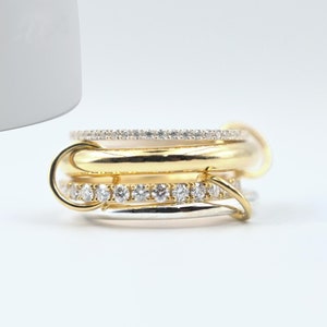 May include: A stack of gold and silver rings with small, clear gemstones. The rings are interlocked, creating a unique and stylish design. The gemstones are set in a row around the rings.