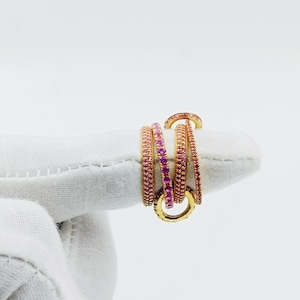May include: Five gold rings with pink gemstones set in a continuous line around the band. The rings are stacked on top of each other.