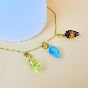 May include: A gold chain necklace with three crystal pendants. The pendants are shaped like teardrops and are in shades of blue, green, and brown.