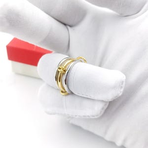 Könnte beinhalten: Ein Satz aus drei goldenen und silbernen Ringen mit einem einzigartigen, ineinandergreifenden Design. Die Ringe sind übereinander gestapelt und aus glattem Metall gefertigt.