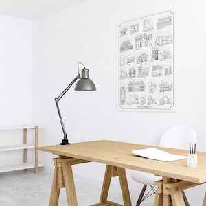 K&ouml;nnte beinhalten: Eine Schwarzwei&szlig;illustration verschiedener Hausstile, gedruckt auf einem wei&szlig;en Poster. Das Poster h&auml;ngt an einer wei&szlig;en Wand in einem Heimb&uuml;ro. Im Vordergrund steht ein Holztisch mit einer Lampe und einem wei&szlig;en Stuhl.