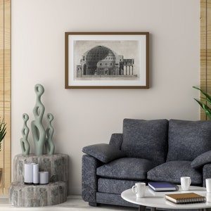 Puede incluir: Un interior de sala de estar con un sof&aacute; gris, una mesa de caf&eacute; con dos tazas blancas y un libro, una planta en maceta y una impresi&oacute;n enmarcada en blanco y negro de un dibujo arquitect&oacute;nico de un edificio con una c&uacute;pula.