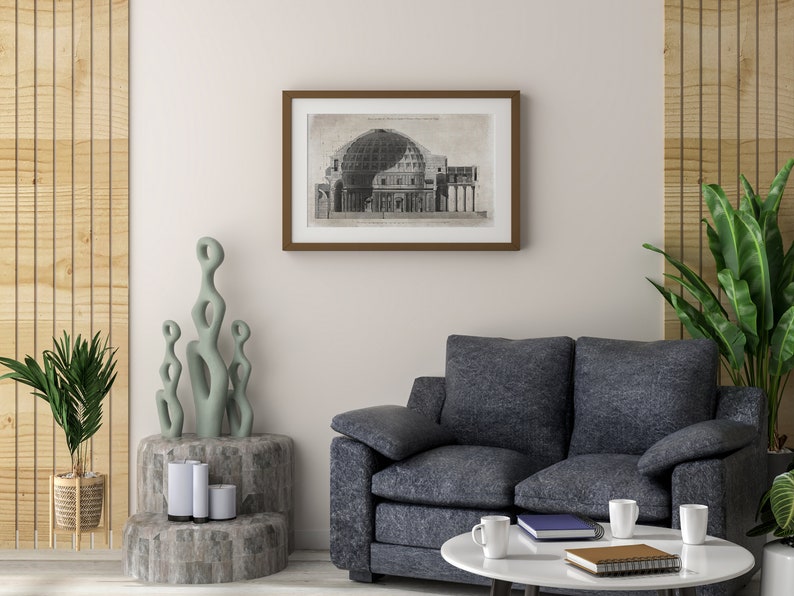 Puede incluir: Un interior de sala de estar con un sof&aacute; gris, una mesa de caf&eacute; con dos tazas blancas y un libro, una planta en maceta y una impresi&oacute;n enmarcada en blanco y negro de un dibujo arquitect&oacute;nico de un edificio con una c&uacute;pula.