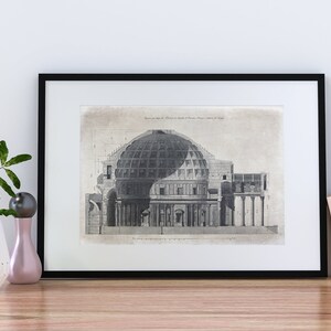 Puede incluir: Impresi&oacute;n vintage en blanco y negro de una secci&oacute;n transversal de un edificio con c&uacute;pula y columnas. La impresi&oacute;n est&aacute; enmarcada en un marco negro y se muestra en un estante de madera con una planta en maceta y otros art&iacute;culos decorativos.