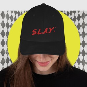 May include: Black baseball cap with a red embroidered "S.L.A.Y." design.