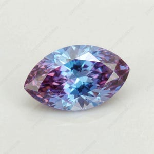 May include: A marquise-cut gemstone with a captivating blend of colors. The gem showcases a gradient of blues and purples, with a central core of vibrant blue that transitions to a deep purple at the edges. The facets create a play of light.