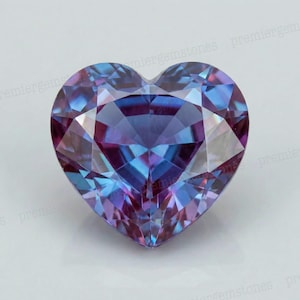 May include: A heart-shaped gemstone with facets, displaying a color gradient of purple, blue, and pink. The gemstone is cut to maximize light reflection, creating a sparkling effect. The gem is set against a white background.