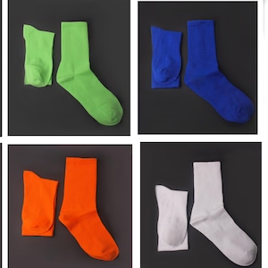 May include: Four pairs of crew socks in green, blue, orange, and white. Each pair includes one folded sock and one unfolded sock, set against a dark grey background. The socks have a ribbed texture.