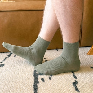 May include: A pair of light green socks with a textured pattern. The socks are worn on a person's feet.