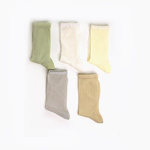 May include: Five pairs of ribbed crew socks in pastel shades: light green, off-white, pale yellow, grey, and tan. The socks are displayed on a white background, highlighting their texture and colours. These socks are suitable for everyday wear.