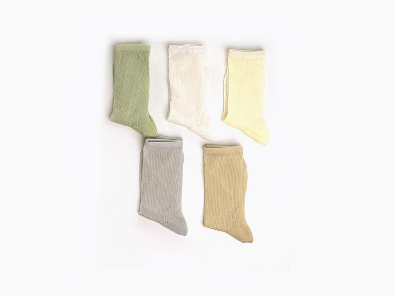 May include: Five pairs of ribbed crew socks in pastel shades: light green, off-white, pale yellow, grey, and tan. The socks are displayed on a white background, highlighting their texture and colours. These socks are suitable for everyday wear.