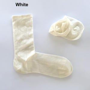 May include: Two off-white socks, one unfolded and one folded, on a white background. The word "White" is at the top left. The socks have a ribbed texture.