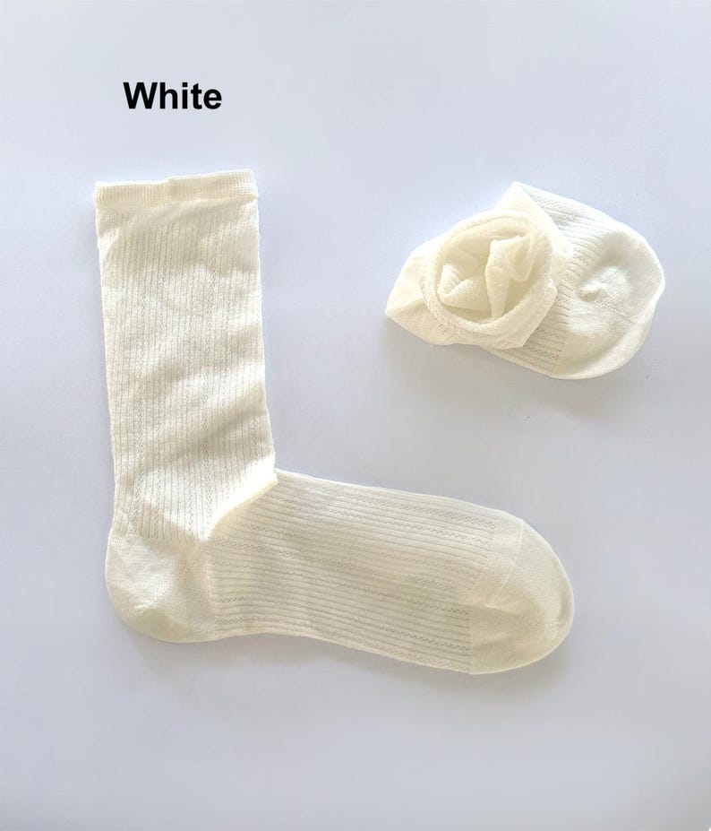May include: Two off-white socks, one unfolded and one folded, on a white background. The word "White" is at the top left. The socks have a ribbed texture.