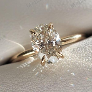 Pode incluir: Um anel de noivado de ouro com um diamante oval em uma caixa branca.