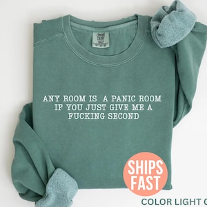 May include: Light green sweatshirt with the text "ANY ROOM IS A PANIC ROOM IF YOU JUST GIVE ME A FUCKING SECOND." The sweatshirt has a crew neck and long sleeves. The words "SHIPS FAST" are in a circle on the bottom right.