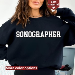Op de afbeelding: Zwart sweatshirt met de tekst "SONOGRAPHER" in witte letters. Het sweatshirt is gemaakt van zacht materiaal.