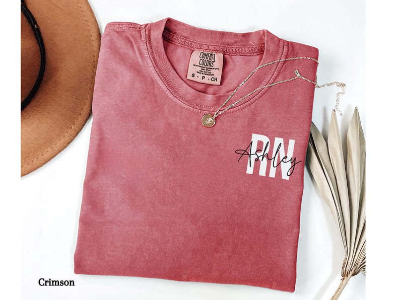 May include: Crimson red t-shirt with a white print that says "Ashley RN".