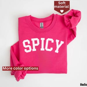 Peut inclure: Sweat-shirt rose avec le mot "SPICY" en lettres blanches. Le sweat-shirt est pli&eacute; en deux et les manches sont retrouss&eacute;es.