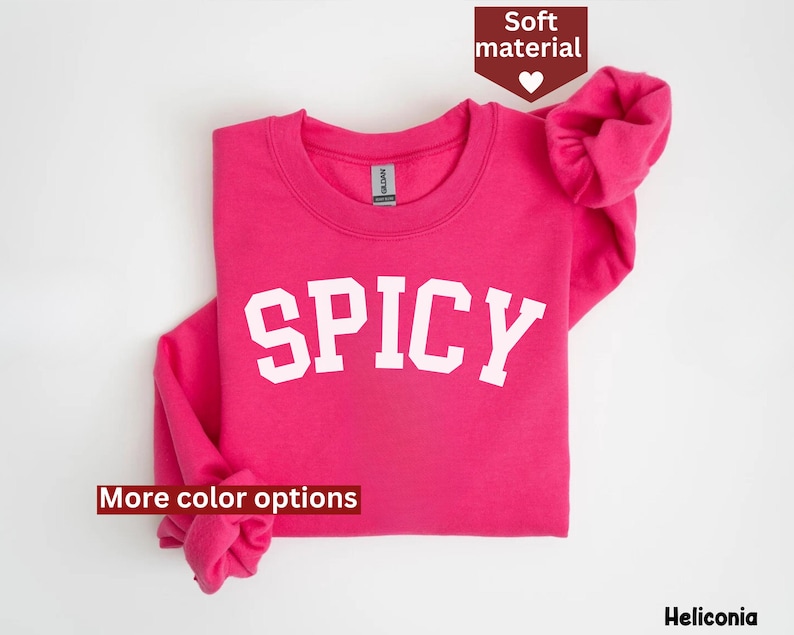 Peut inclure: Sweat-shirt rose avec le mot "SPICY" en lettres blanches. Le sweat-shirt est pli&eacute; en deux et les manches sont retrouss&eacute;es.