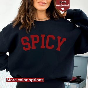 Peut inclure: Sweat-shirt noir avec le mot "SPICY" imprim&eacute; en lettres rouges. Le sweat-shirt a des manches longues et un col rond.
