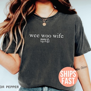 May include: Dark gray t-shirt with the text "wee woo wife" above a small illustration of a fire truck. The shirt is a pepper color.