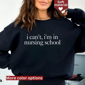 May include: Black sweatshirt with the text "i can't, i'm in nursing school" in white. The sweatshirt has a crew neck and long sleeves. The words "Soft material" are in a red banner in the top right corner. The words "More color options" and "Black" are in a red banner at the bottom.