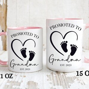 K&ouml;nnte beinhalten: Zwei wei&szlig;e Keramikbecher mit rosa R&auml;ndern. Die Becher haben schwarzen Text, der "Bef&ouml;rdert zur Oma Est. 2023" lautet, mit einem schwarzen Herzen und einem Fu&szlig;abdruckdesign. Der Becher links ist 11 oz und der Becher rechts ist 15 oz.