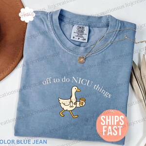 Puede incluir: Una camiseta de color azul vaquero con un gr&aacute;fico de un ganso blanco que lleva un estetoscopio y sostiene una taza de caf&eacute;. El texto sobre el ganso dice off to do NICU things. La camiseta tiene una etiqueta de la marca Comfort Colors visible.