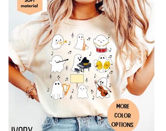 May include: Ivory-colored t-shirt featuring a musical ghost design. The ghosts are playing various instruments, including a trumpet, saxophone, drums, piano, cymbals, harp, and violin. The shirt also has the words "SOFT material" and "MORE COLOR OPTIONS".