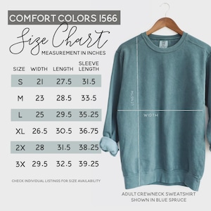 May include: Blue spruce adult crewneck sweatshirt displayed on a wooden hanger. The image includes a size chart with measurements in inches for width, length, and sleeve length. The size chart includes sizes S, M, L, XL, 2X, and 3X.