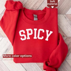 Puede incluir: Sudadera roja con la palabra "SPICY" impresa en blanco en la parte delantera. La sudadera tiene cuello redondo y mangas largas.