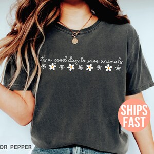 K&ouml;nnte beinhalten: Dunkelgraues T-Shirt mit dem wei&szlig;en Schriftzug "it's a good day to save animals", verziert mit wei&szlig;en G&auml;nsebl&uuml;mchen. Ein l&auml;ssiger, bequemer Kleidungsstil.