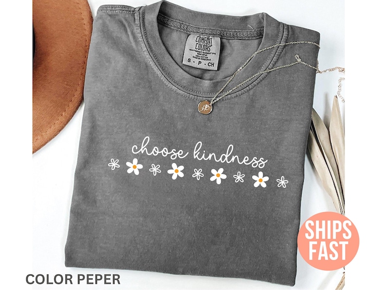 May include: A gray Comfort Colors t-shirt with the words "choose kindness" in white script, and white daisy graphics. A silver necklace with a pendant is on the shirt. The shirt has a small tag at the neckline.