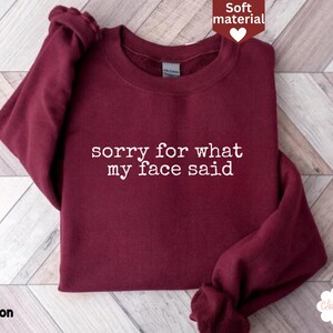 May include: Maroon crewneck sweatshirt with the text "sorry for what my face said" in white. The sweatshirt is made of a soft material. The word "marron" is printed in the bottom left corner.
