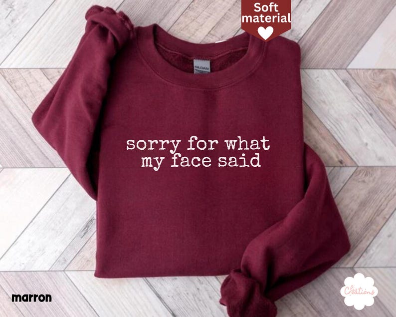 May include: Maroon crewneck sweatshirt with the text "sorry for what my face said" in white. The sweatshirt is made of a soft material. The word "marron" is printed in the bottom left corner.