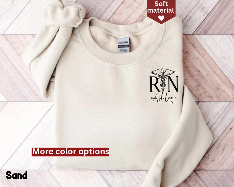 May include: A cream-colored sweatshirt with a black graphic of a medical caduceus and the text "RN Ashley".