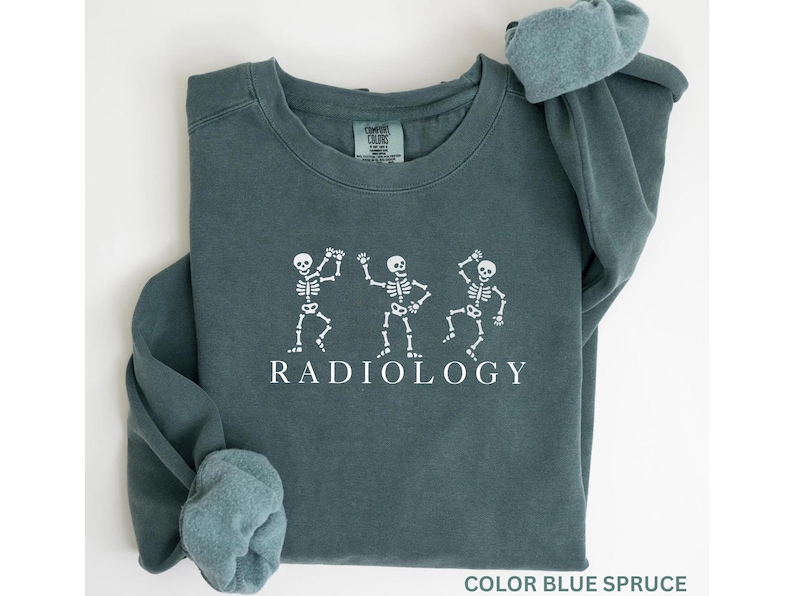 May include: Blue spruce-colored sweatshirt with white skeleton graphics dancing. The word "RADIOLOGY" is printed in white below the skeletons. The sweatshirt has a crew neck and long sleeves.