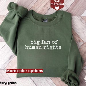May include: Military green sweatshirt with the text "big fan of human rights" in white. The long-sleeved top has a crew neck and a soft material. The image also includes the words "More color options" and "Soft material".