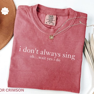 Könnte beinhalten: Karmesinrotes T-Shirt mit dem weißen Text "i don't always sing oh...wait yes i do". Das Shirt hat einen Rundhalsausschnitt und kurze Ärmel. Eine silberne Halskette mit Anhänger liegt auf dem Shirt.