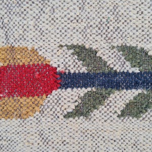 May include: Close-up of a woven textile with a repeating pattern. The design features a colorful arrow in shades of red, gold, blue, and green. The arrow is centered on a neutral background.